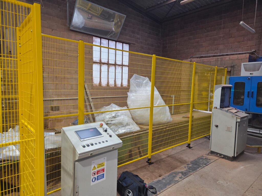 Machine industrielle sécurisée par une cloison grillagée avec panneaux jaunes